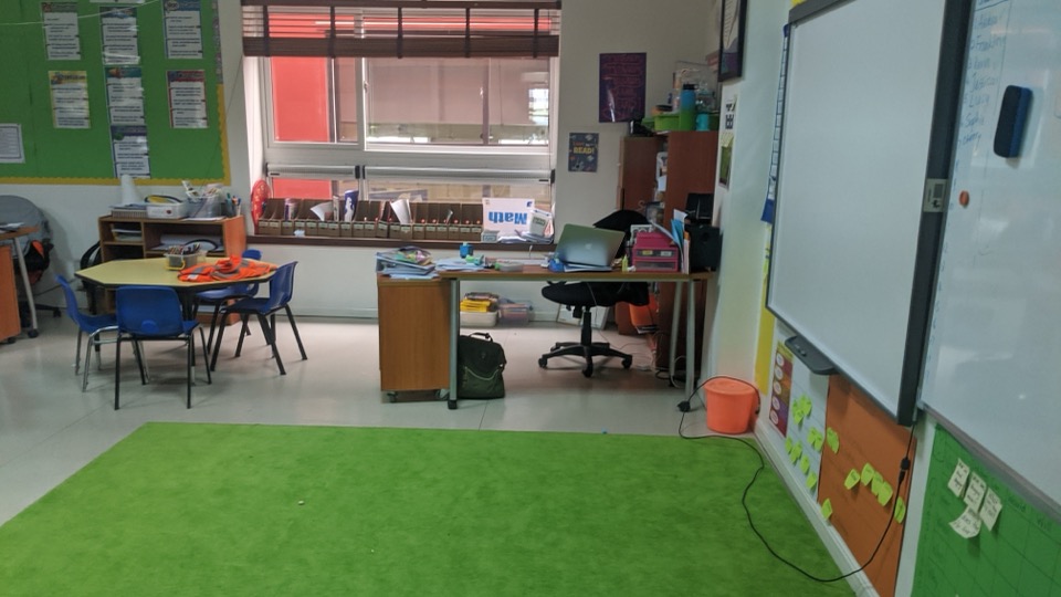 An empty classroom with a green carpet, set up for the day